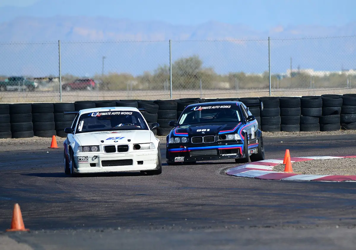 Two Ultimate Auto Works BMW E36 race cars cornering nose to tail on a desert race track